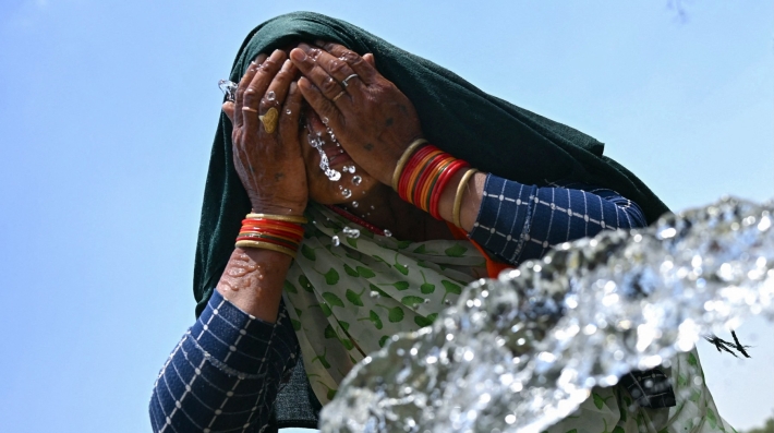 A woman washes her face with water to cool off 