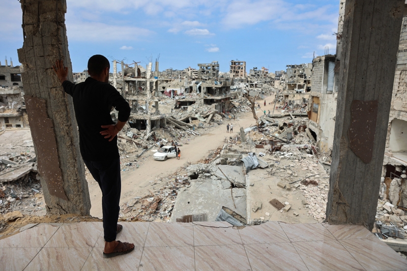 A man stands in building overlooking a rubble-strewn street