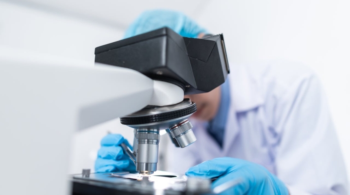 A scientist in a lab coat using a microscope 