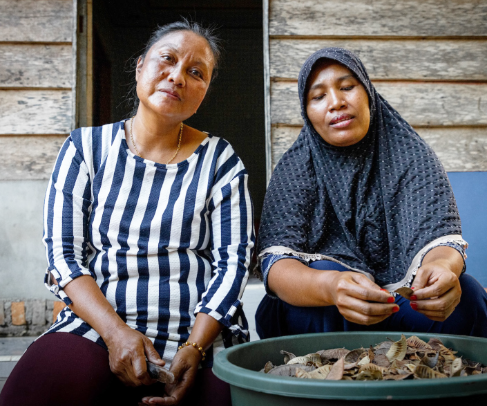 Two women sitting on a bench and holding a bowl full of seeds  