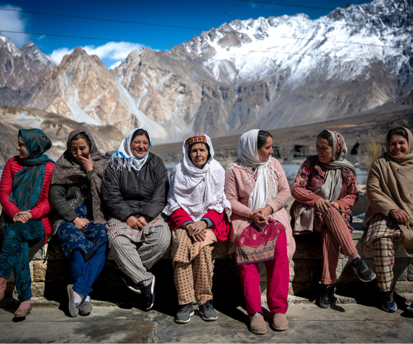 Seven women sitting on a bench with snow-capped mountains in the background  